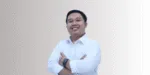 Seseorang mengenakan kemeja putih dengan sikap percaya diri, berdiri dengan tangan disilangkan di depan tubuhnya, di latar belakang yang bergradasi halus.